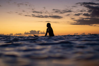 Rear view of woman standing on beach against sky during sunset