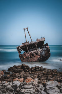 Sailboat on rocks by sea against sky