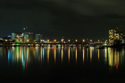 Illuminated buildings by river against sky at night