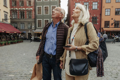 Amazed senior couple looking up while standing together in city