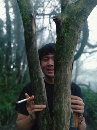 Portrait of smiling man holding tree trunk in forest
