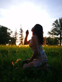Side view of woman holding dandelion while sitting on field
