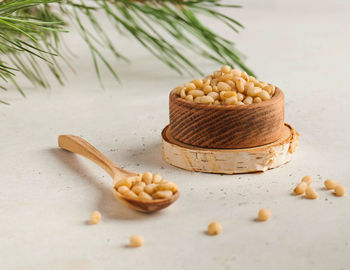 Pine nuts in a wooden bowl and in a wooden spoon on the background of a coniferous branch. 