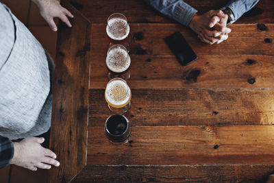 Directly above shot of bartender with various beer glasses by customer at wooden table