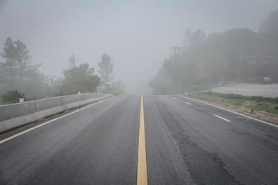 Empty road by trees against sky