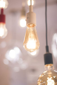 Close-up of illuminated light bulb hanging from ceiling