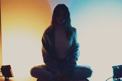 Portrait of young woman sitting against wall