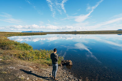 Rear view of man standing by river against sky