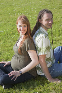 Portrait of smiling pregnant woman sitting with husband on grassy field