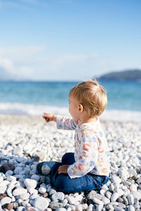 Boy sitting on pebbles at beach