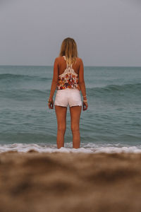 Rear view of young woman standing at beach against clear sky