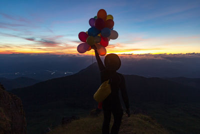 Man with balloons at field against sky during sunset