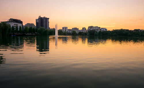 Scenic view of lake by buildings against sky during sunset