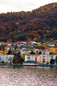 Buildings by river against sky during autumn