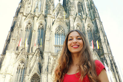 Portrait of smiling young woman standing against cologne cathedral