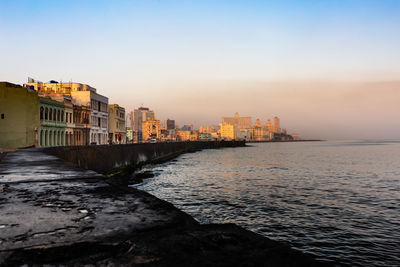 Sea by buildings against sky during sunset
