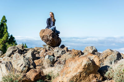 Low angle view of woman sitting on rock by sea against clear sky