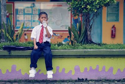 School boy drinking water while sitting on retaining wall