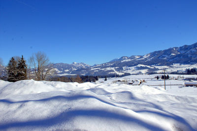 Snow covered landscape against clear blue sky