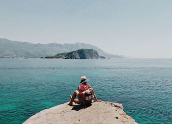 Man sitting on rock by sea against clear sky