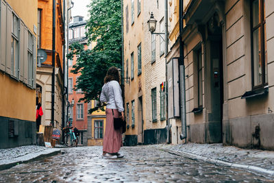 Rear view of woman walking on footpath amidst buildings