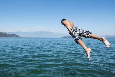Shirtless young man jumping in sea against blue sky