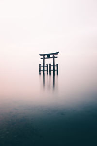 Shrine in lake against sky during sunset