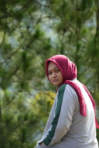 Portrait of young woman standing against trees