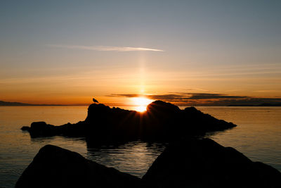 Silhouette rocks in sea against sky during sunset