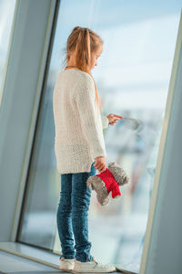 Full length of girl standing by glass window