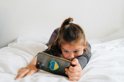 Young woman using mobile phone while lying on bed at home