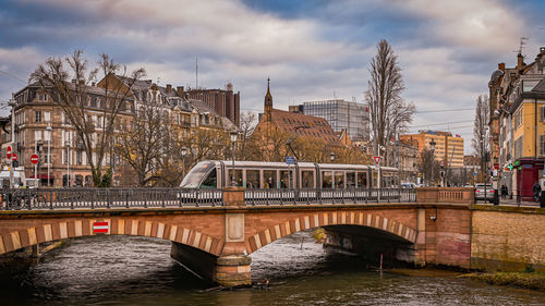 Bridge over river in city against cloudy sky