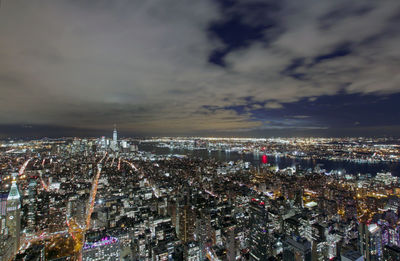 Illuminated cityscape against cloudy sky at night