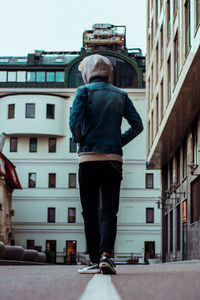 Rear view of man walking on street against building