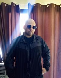 Man wearing sunglasses standing against curtain