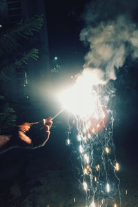 Cropped hand holding lit sparkler at night