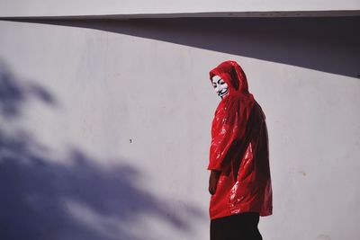 Side view of young woman standing against red wall