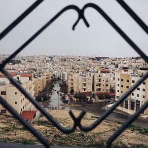 Cityscape seen through chainlink fence against sky