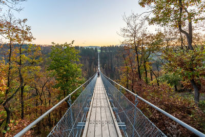 Footbridge amidst trees against sky during autumn