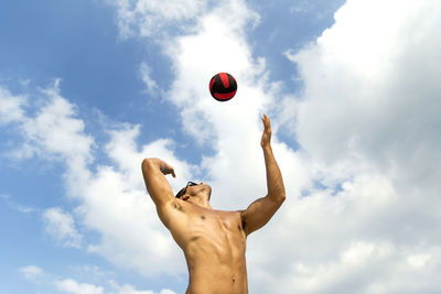 Low angle view of fit shirtless young man playing with ball against sky