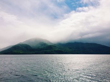 Scenic view of lake by mountain against cloudy sky
