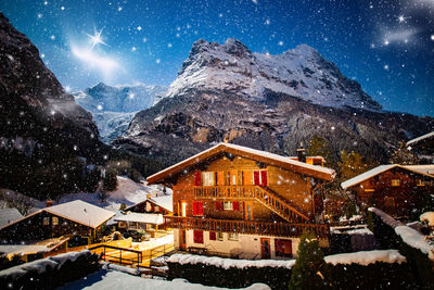 Snow covered houses by mountain against sky at night