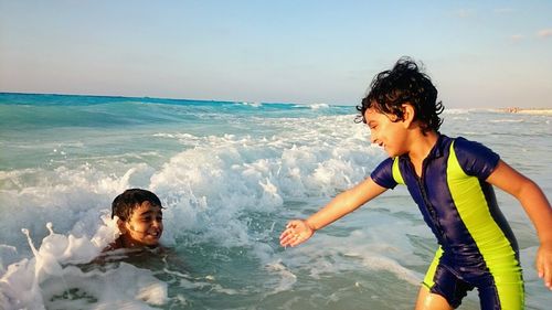 Boy giving helping hand to friend in sea