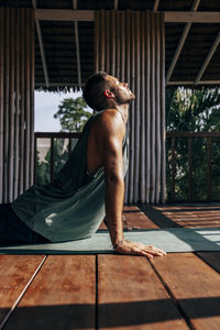 Side view of man doing cobra pose on yoga mat over hardwood floor at wellness resort