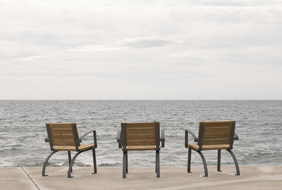 Empty chairs and table by sea against sky