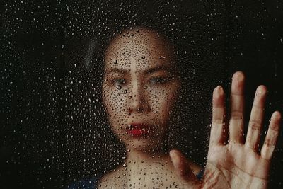 Close-up portrait of woman seen through wet window