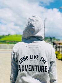 Rear view of person wearing hooded shirt with text against cloudy sky