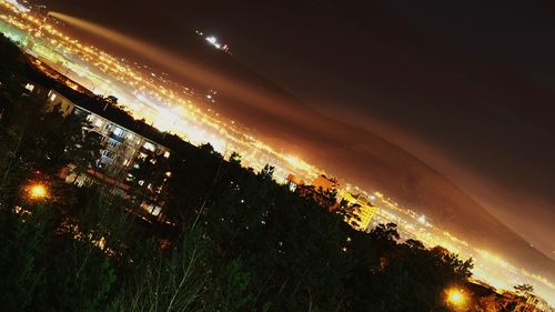 Aerial view of illuminated city by sea against sky at sunset