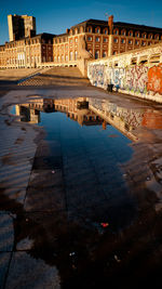 Puddle by historic buildings against clear sky