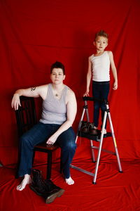 Full length of mother and son with chairs against red fabric